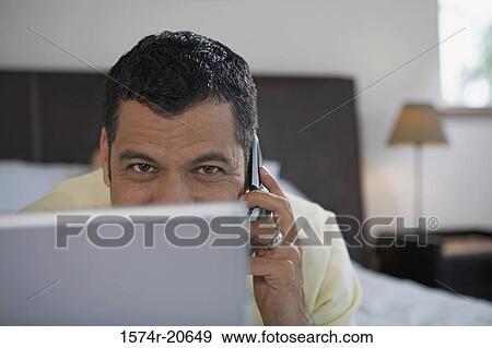 Portrait of a mature man lying in front of a laptop and talking on a mobile phone View Large Photo Image Stock Photo - Portrait of a mature man lying in front of a laptop and talking on a mobile phone. Fotosearch