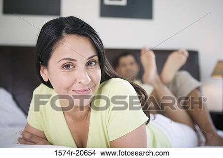 Portrait of a mature woman lying in the bed with a mature man reclining behind her View Large Photo Image Picture - Portrait of a mature woman lying in the bed with a mature man reclining behind her. Fotosearch