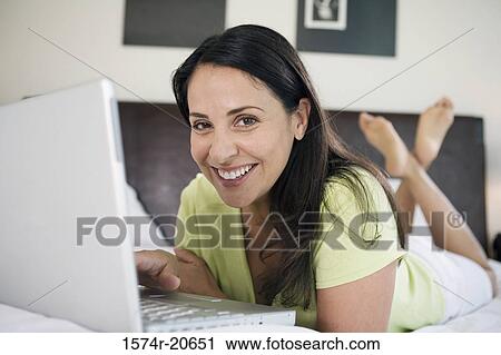 Portrait of a mature woman lying in the bed and using a laptop View Large Photo Image Stock Image - Portrait of a mature woman lying in the bed and using a laptop. Fotosearch