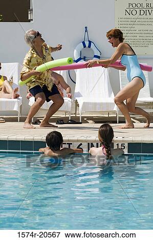 Stock Photo - Side profile of a senior couple playing at poolside. Fotosearch