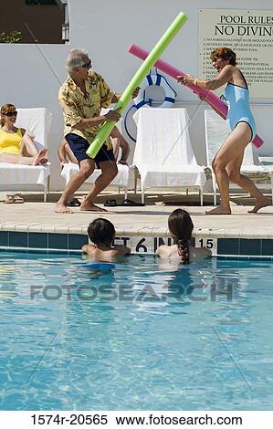 Stock Photography - Side profile of a senior couple playing at poolside. Fotosearch