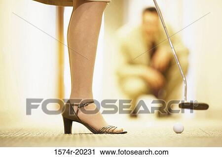 Low section view of a businesswoman playing golf with a businessman crouching in the background View Large Photo Image Stock Image - Low section view of a businesswoman playing golf with a businessman crouching in the background. Fotosearch