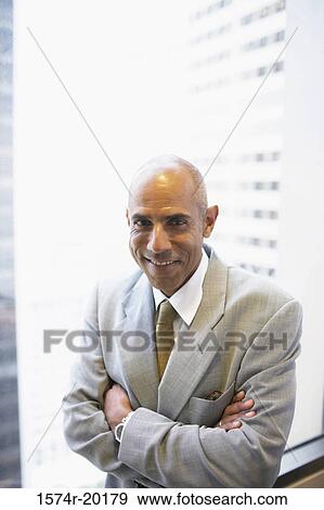 Portrait of a businessman standing with his arms crossed in an office View Large Photo Image Stock Photo - Portrait of a businessman standing with his arms crossed in an office. Fotosearch