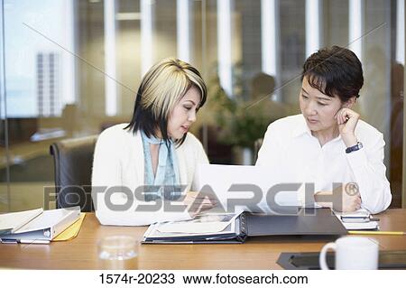Stock Image - Two businesswomen talking in an office. Fotosearch