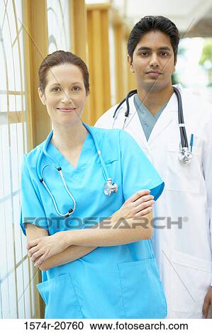 Stock Image - Portrait of a female doctor smiling and a male doctor standing behind her. Fotosearch