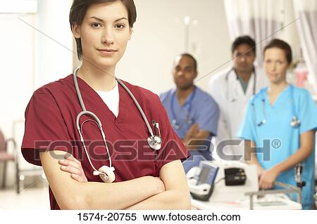 Stock Photography - Portrait of a female doctor standing with her arms crossed and her colleagues in the background. Fotosearch