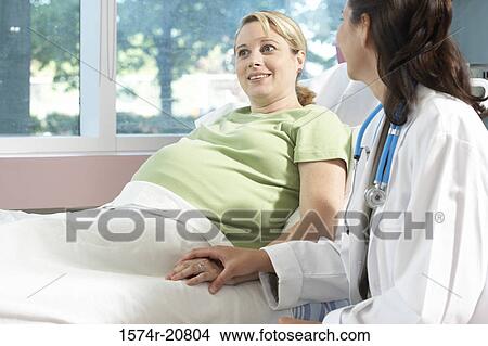Pregnant woman reclining on the bed with a female doctor sitting beside her View Large Photo Image Picture - Pregnant woman reclining on the bed with a female doctor sitting beside her. Fotosearch