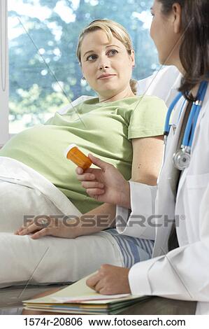 Stock Photograph - Side profile of a female doctor giving a bottle of pills to a pregnant woman. Fotosearch