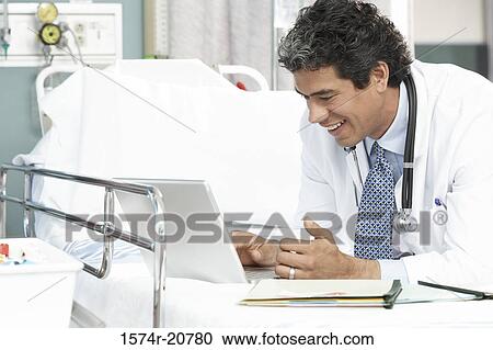Stock Image - Side profile of a male doctor using a laptop. Fotosearch