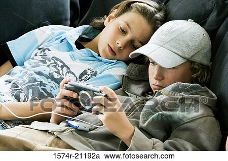 Close-up of a boy playing a handheld video game with another boy lying beside him View Large Photo Image Stock Image - Close-up of a boy playing a handheld video game with another boy lying beside him. Fotosearch