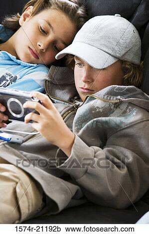 Close-up of a boy playing a handheld video game with another boy lying beside him View Large Photo Image Stock Image - Close-up of a boy playing a handheld video game with another boy lying beside him. Fotosearch
