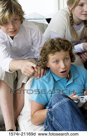 Stock Image - Close-up of a boy playing a video game with his friends sitting behind him. Fotosearch