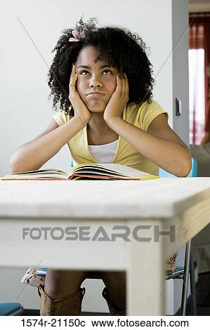Stock Image - Close-up of a girl sitting at a table with a book in front of her. Fotosearch