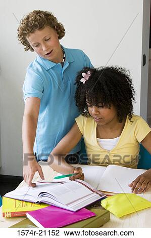 Girl doing her homework with a boy standing near her View Large Photo Image Stock Image - Girl doing her homework with a boy standing near her. Fotosearch