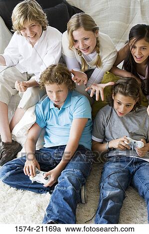 High angle view of a boy and a girl playing a video game with their friends sitting behind them View Large Photo Image Stock Image - High angle view of a boy and a girl playing a video game with their friends sitting behind them. Fotosearch