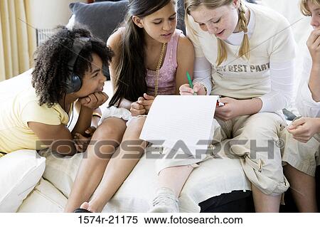 Stock Photography - High angle view of a girl writing on a notepad with her friends sitting beside her. Fotosearch
