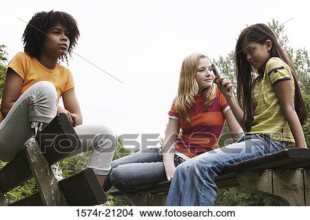 Low angle view of three girls sitting on benches View Large Photo Image Picture - Low angle view of three girls sitting on benches. Fotosearch