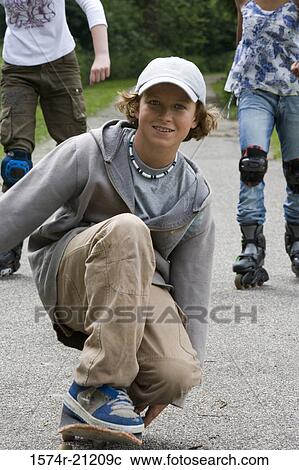 Stock Image - Portrait of a boy crouching on a skateboard and two girls inline skating behind him. Fotosearch