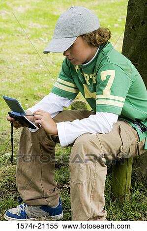 Side profile of a boy using a personal data assistant in a park View Large Photo Image Stock Photography - Side profile of a boy using a personal data assistant in a park. Fotosearch
