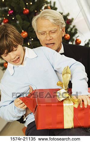 Stock Photography - Close-up of a boy unwrapping a Christmas present with his grandfather. Fotosearch