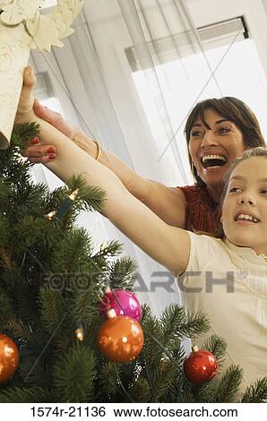 Stock Photograph - Close-up of a grandmother and her granddaughter decorating a Christmas tree. Fotosearch