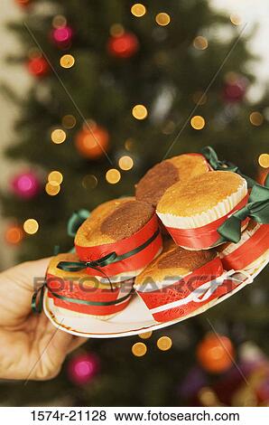 Stock Photo - Close-up of a person's hand holding cupcakes on a plate. Fotosearch