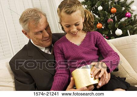 Stock Image - Close-up of a senior man with his granddaughter holding a Christmas present and smiling. Fotosearch