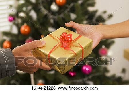 Stock Photo - Close-up of two people's hands holding a Christmas present. Fotosearch