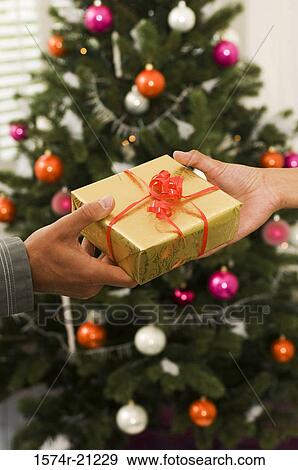 Stock Photo - Close-up of two people's hands holding a Christmas present. Fotosearch