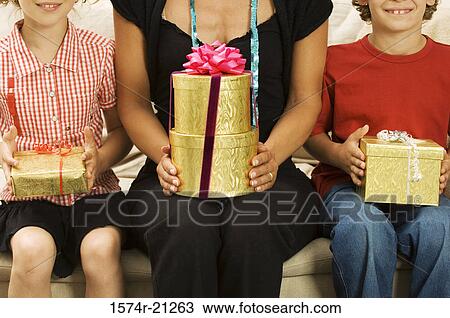 Mid section view of a woman with her son and daughter sitting on a couch holding Christmas presents View Large Photo Image Stock Image - Mid section view of a woman with her son and daughter sitting on a couch holding Christmas presents. Fotosearch