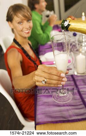Portrait of a young woman holding a champagne flute with a mid adult man sitting in the background View Large Photo Image Picture - Portrait of a young woman holding a champagne flute with a mid adult man sitting in the background. Fotosearch