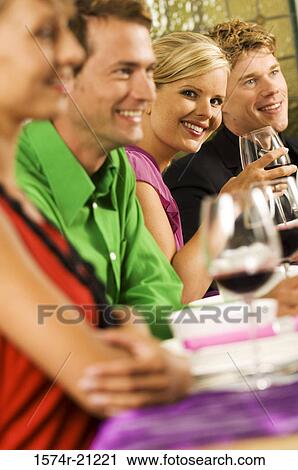 Portrait of a young woman with her friends smiling at a dining table View Large Photo Image Stock Image - Portrait of a young woman with her friends smiling at a dining table. Fotosearch