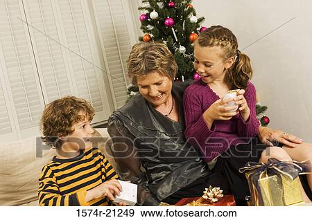 Senior woman sitting with her grandson and granddaughter opening Christmas presents View Large Photo Image Stock Photo - Senior woman sitting with her grandson and granddaughter opening Christmas presents. Fotosearch