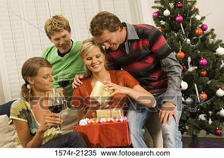 Stock Photography - Young woman opening a Christmas present with her three friends. Fotosearch