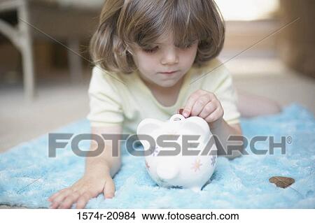 Close-up of a girl inserting a coin into a piggy bank View Large Photo Image Picture - Close-up of a girl inserting a coin into a piggy bank. Fotosearch