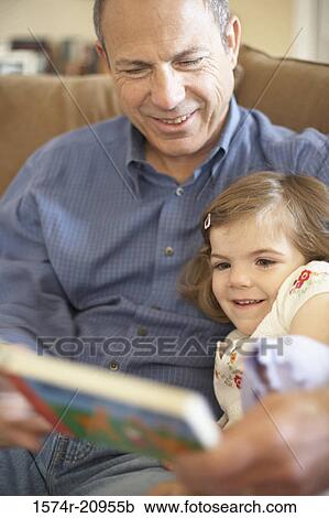 Stock Image - Close-up of a girl sitting with her grandfather and reading a book. Fotosearch