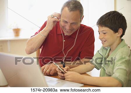 Close-up of a mature man wearing headphones with his grandson sitting beside him View Large Photo Image Stock Image - Close-up of a mature man wearing headphones with his grandson sitting beside him. Fotosearch