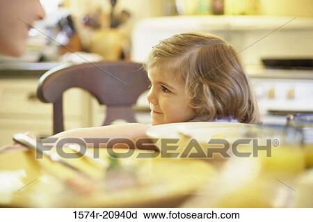 Stock Image - Girl sitting at a dining table and smiling. Fotosearch