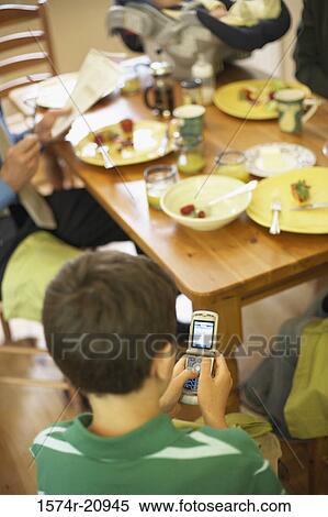 Stock Photography - High angle view of a boy sitting at a dining table and using a mobile phone. Fotosearch