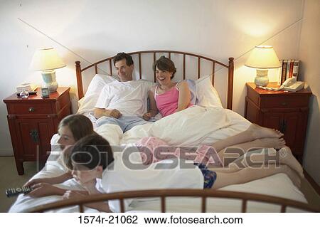 High angle view of a mid adult couple with their son and daughter lying in the bed and watching TV View Large Photo Image Stock Image - High angle view of a mid adult couple with their son and daughter lying in the bed and watching TV. Fotosearch