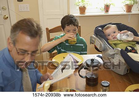 Stock Image - High angle view of a mid adult man with his two sons sitting at a dining table. Fotosearch