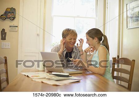 Mature woman wearing headphones and listening to music with her granddaughter sitting beside her View Large Photo Image Stock Image - Mature woman wearing headphones and listening to music with her granddaughter sitting beside her. Fotosearch