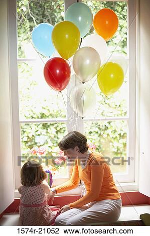 Rear view of a girl sitting with her mother on a window ledge View Large Photo Image Stock Image - Rear view of a girl sitting with her mother on a window ledge. Fotosearch