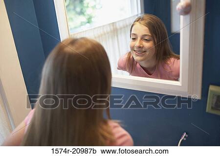 Stock Image - Reflection of a teenage girl looking at her teeth in a mirror. Fotosearch