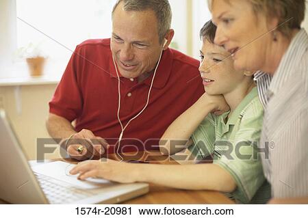 Stock Image - Side profile of a boy sitting with his grandparents and using a laptop. Fotosearch
