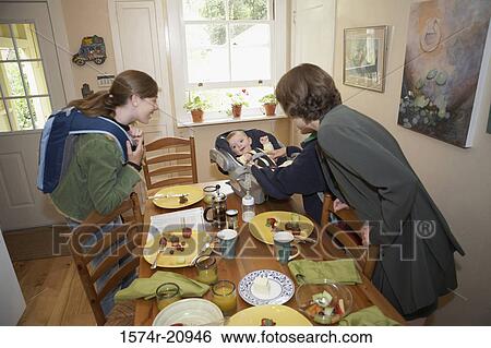 Side profile of a mid adult woman and her daughter cuddling a baby boy at a dining table View Large Photo Image Stock Photograph - Side profile of a mid adult woman and her daughter cuddling a baby boy at a dining table. Fotosearch