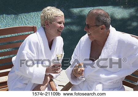 Stock Image - Close-up of a mature couple holding champagne flutes at poolside. Fotosearch