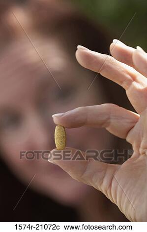 Stock Image - Close-up of a mature woman showing a pill. Fotosearch