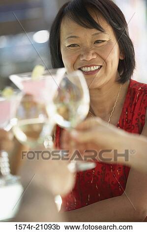 Stock Image - Human hands toasting with glasses and a mature woman smiling in the background. Fotosearch