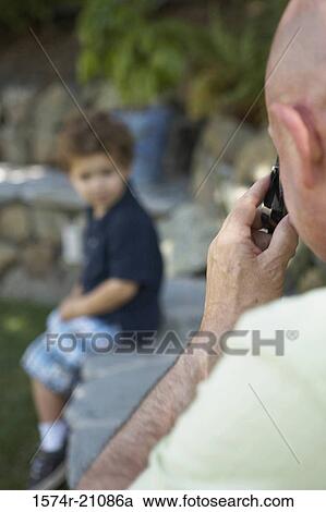 Rear view of a mature man taking a photograph of his grandson View Large Photo Image Stock Image - Rear view of a mature man taking a photograph of his grandson. Fotosearch